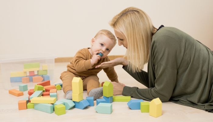 Mom plays with baby in the room, child put wooden block in his mouth.