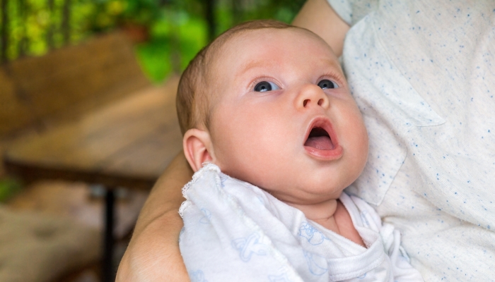 Newborn baby with open mouth is in arms of his mother and looks up.