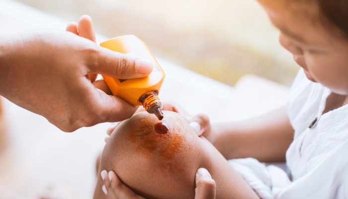 Parent helping her child perform first aid knee injury after she has been an accident.