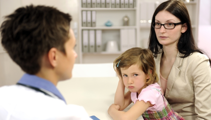 Pediatrician talking to mother and upset child at office.