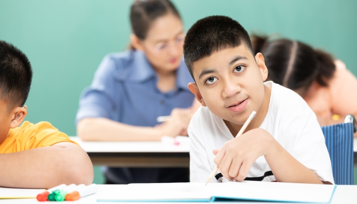 Portrait asian disabled kids or autism child learning looking and writing at desks in classroom.