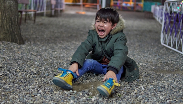 Sad and upset child latin boy shouting and crying sitting on the pebble floor in a amusement park.