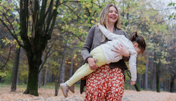 Single mother and daughter spinning in autumn day at the park.