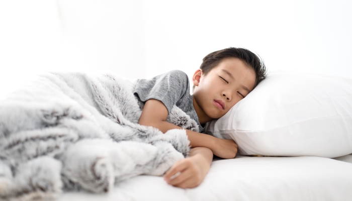 Thai boy sleeping on a white bed in a bedroom.