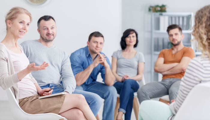 Therapist congratulating young woman on her progress in therapy and happy family in the background.