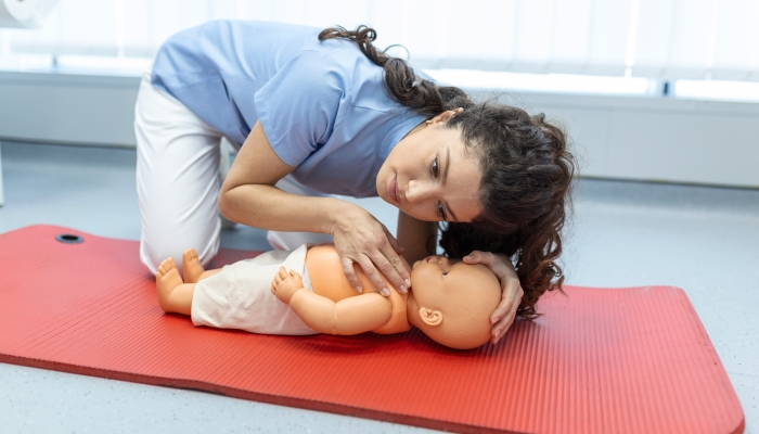 Woman performing CPR on baby training doll with one hand compression.
