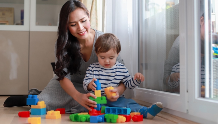 Young Asian mother playing with construction blocks toy with her baby at home.