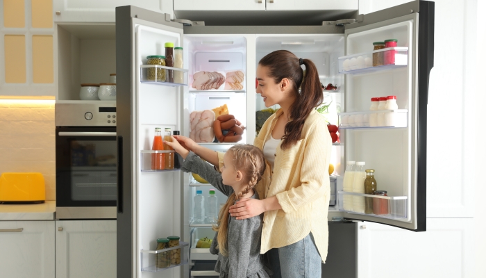 Young mother with daughter taking juice out of refrigerator in kitchen.