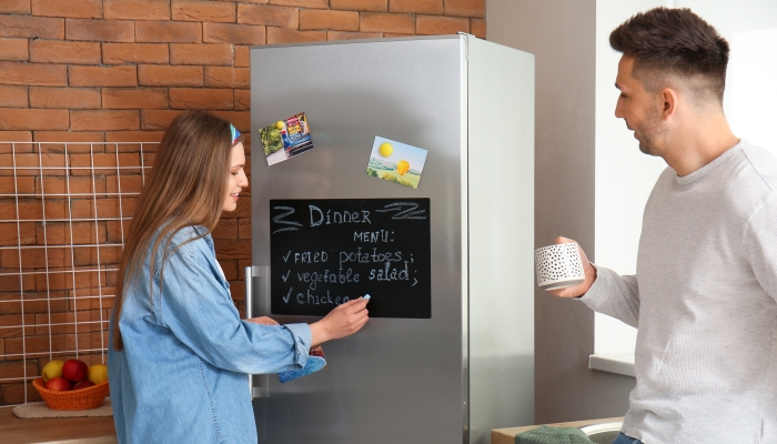 Young woman writing menu on chalkboard in kitchen.