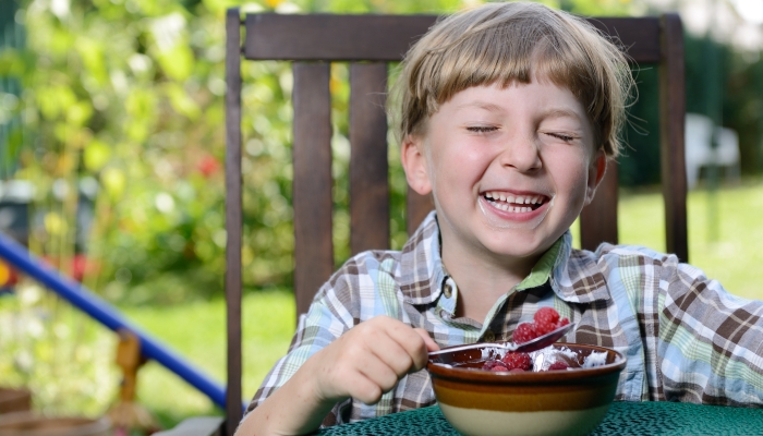 A young boy eating a tasty raspberry with yogurt.