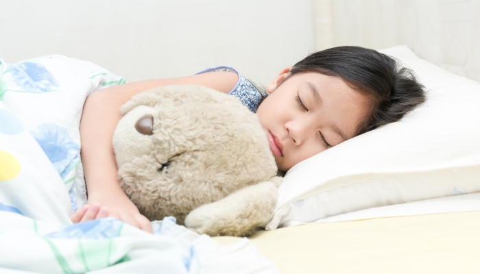 cute little asian girl sleep and hug teddy bear on bed in the bedroom.