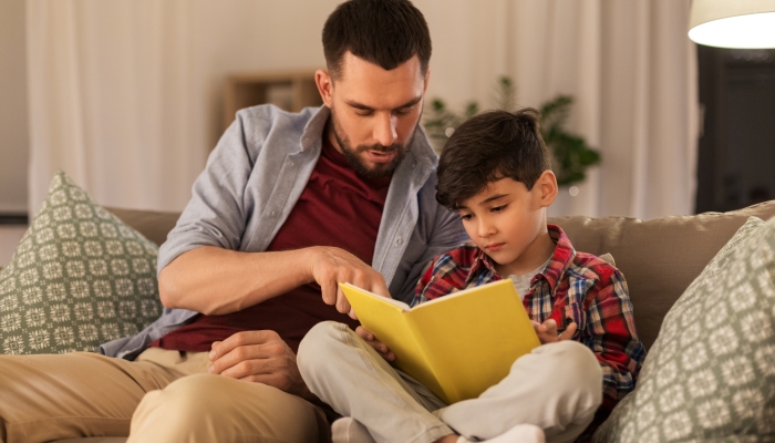 Father and little son reading book on sofa at home.