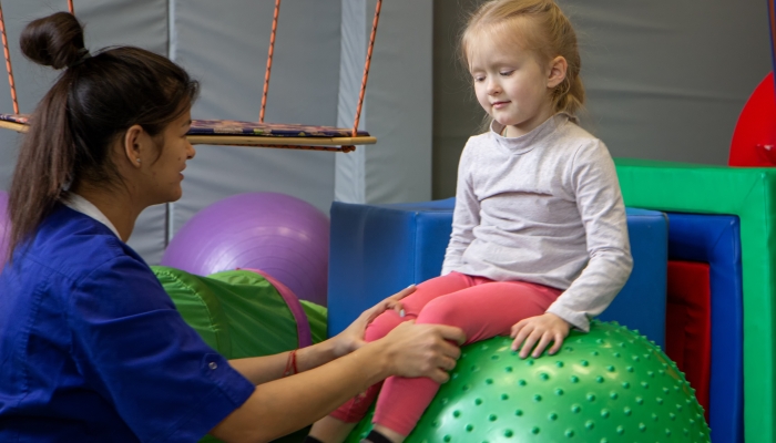 Little girl sitting on big gym ball working with physiotherapist