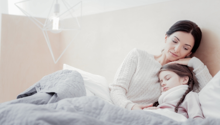 Mother lying in bed while embracing her little autistic daughter.