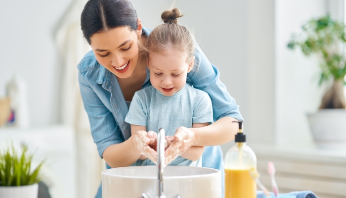 A cute little girl and her mother are washing their hands.