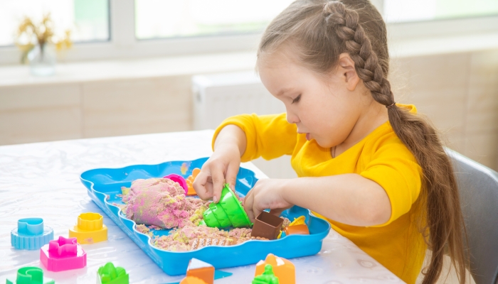 A little European girl plays with beads in the colored sand.