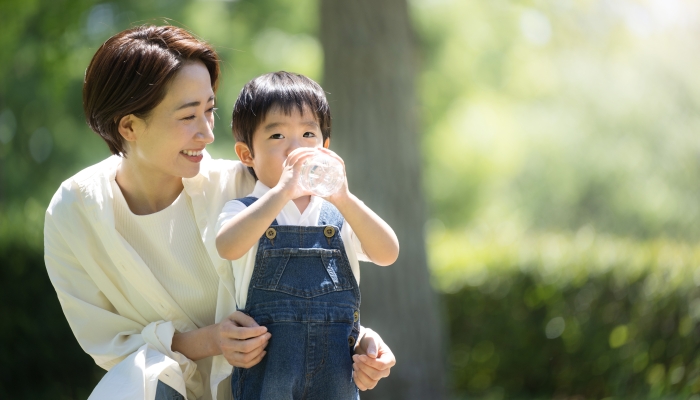 A mother gives her child a drink of water in a fresh green park.