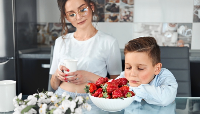 A sad boy sits at the table and looks at a plate with strawberries.