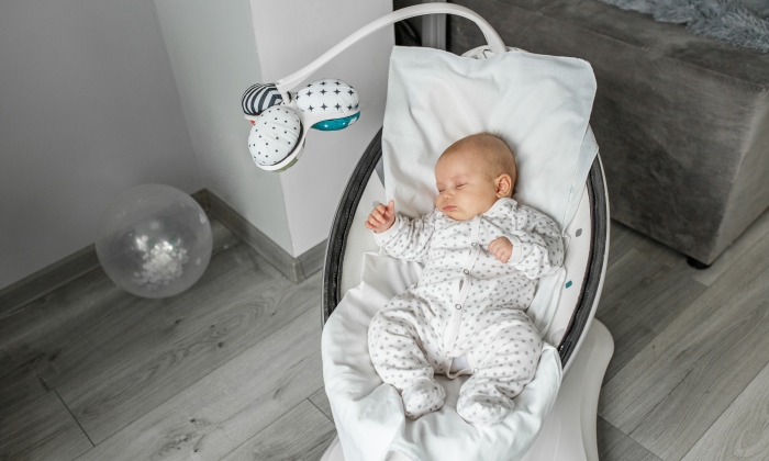 Adorable baby sleeps in baby swing in room.