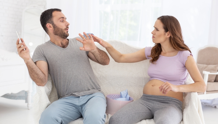 Angry pregnant woman shouting at man and sitting on sofa.