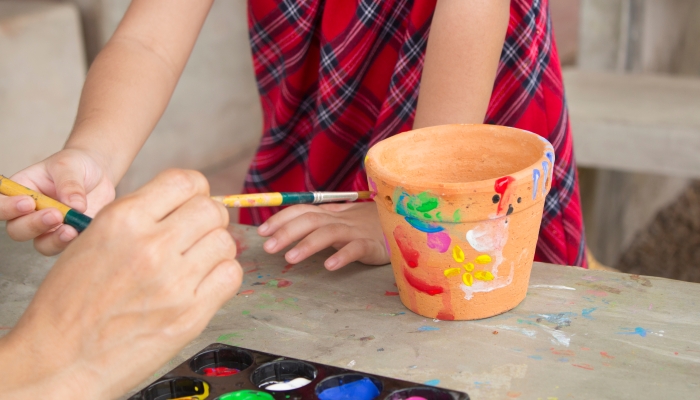 Asian little girl painting flowers pots on the garden with family on holiday.