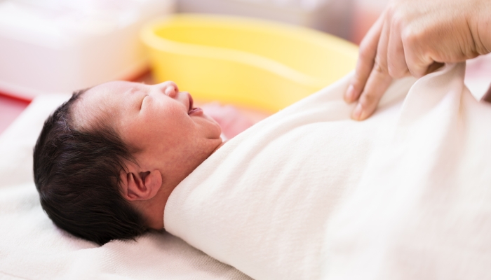 Asian new born baby smiling while mother's hand swaddling her body with white blanket after her first shower.