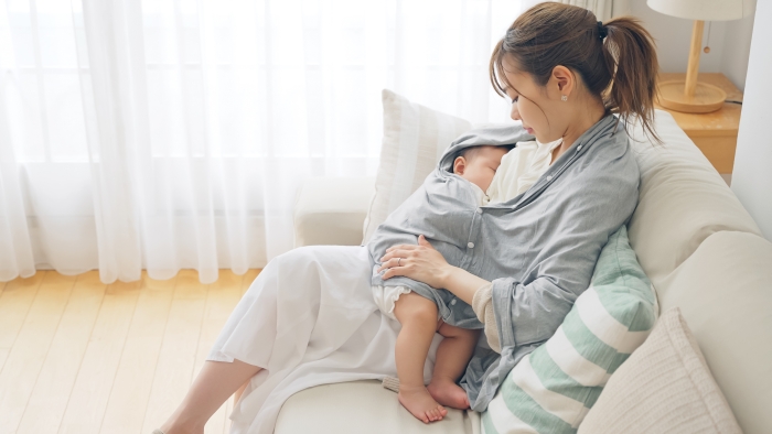 Asian woman breastfeeding baby using a breastfeeding cape.