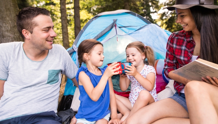 Beautiful young family with daughters camping in forest.