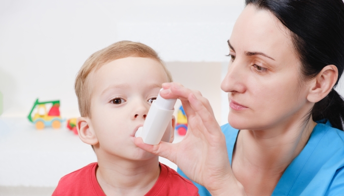 Causian little boy making inhalation with nebulizer at home.