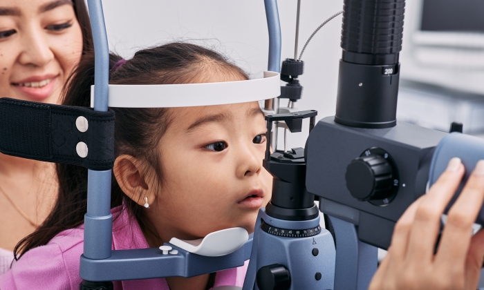Checking little Korean girl's eyesight with binocular slit lamp in ophthalmology clinic.