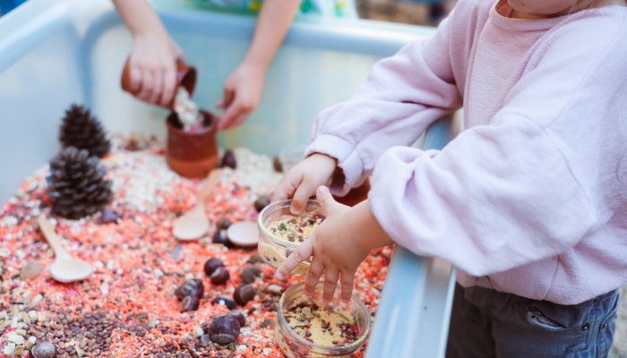 Children playing at a sensory bin with coloured grains, pretending to cook.