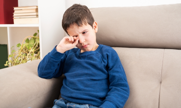 Close up of child scratching itchy eye at home.