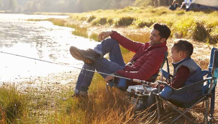 Father and son on a camping trip fishing by a lake.