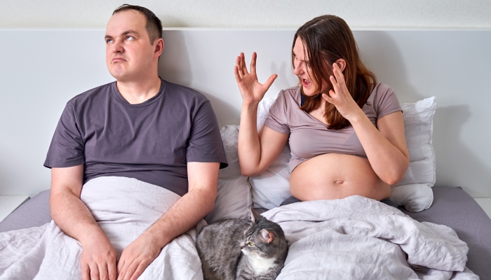 Husband and wife quarrel, pregnant woman yells at man in home bed.