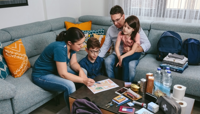 Mother explaining to her family the assembly point map while preparing emergency backpacks.