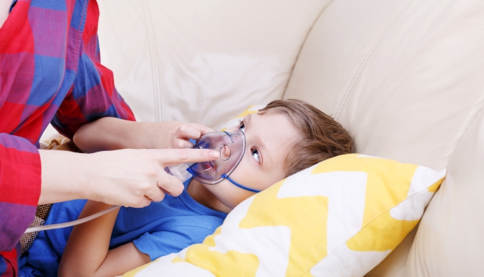 Mother holds a nebulizer mask in the boy's face during inhalation.