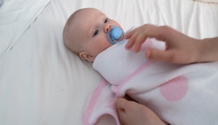 Mother preparing her newborn baby for rest swaddling in a blanket.