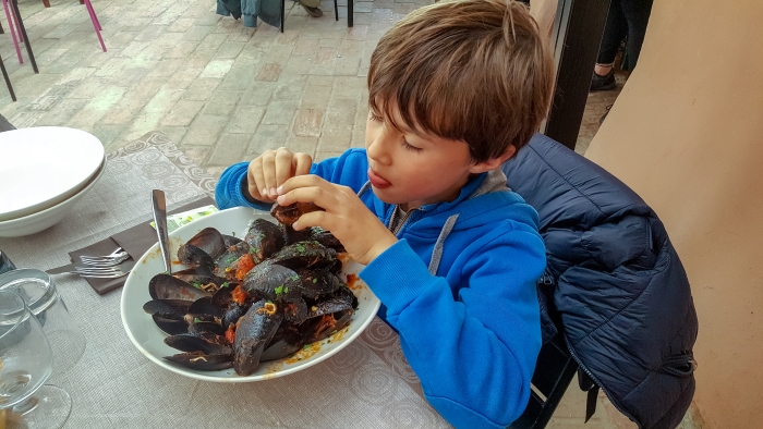 Plate of mussels served to a child who opens them with his hands.