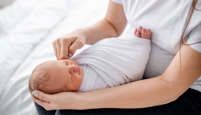 Swaddled newborn baby sleeping in hands of her mother at home.