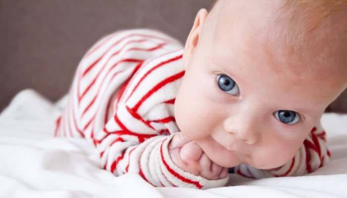 Sweet baby boy dressed in a striped sleepsuit lying with the fists under his head.