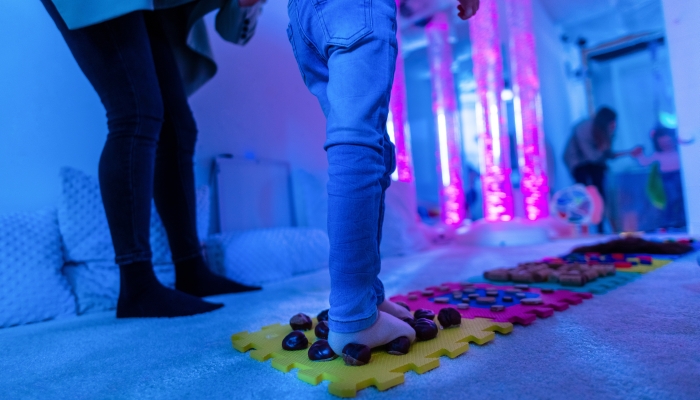Therapist helping a child living with cerebral palsy successfully improve her walking ability during therapy session in a sensory room.