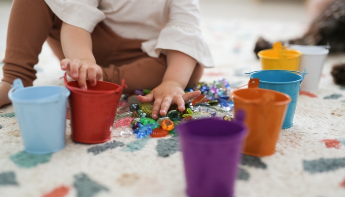 Toddler girl plays with beads and multicolored buckets.
