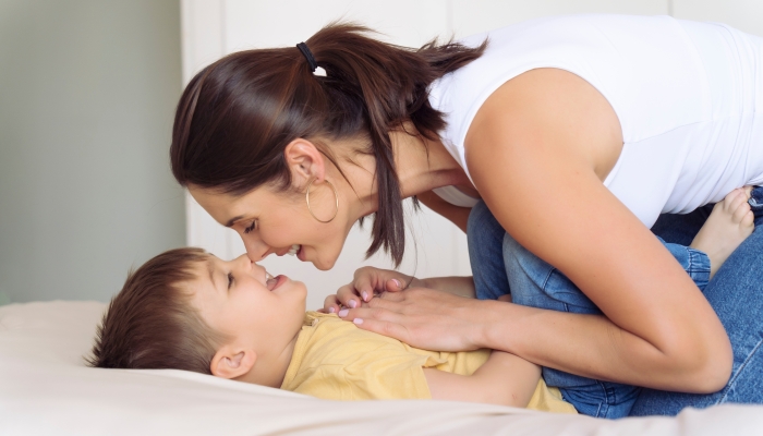 Woman next to her adorable little son playing on bed in room.