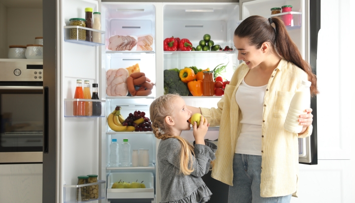 Young mother and her daughter with products near open refrigerator in kitchen.