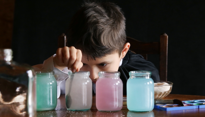 Boy at the table with jars of colored liquid.