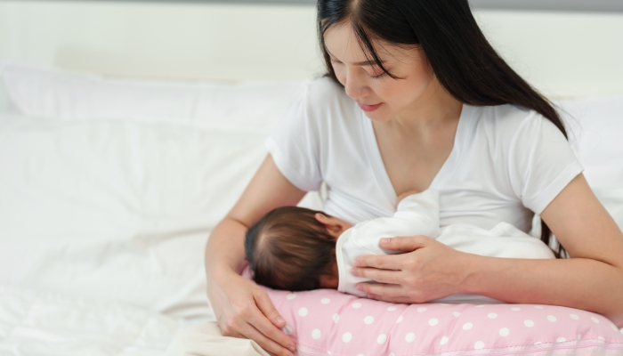 Mother breastfeeding newborn baby on a support pillow cushion.