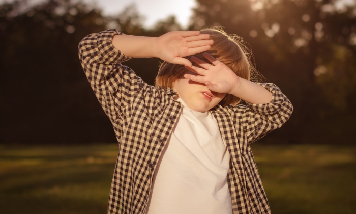 Boy covering eyes by hand from sunlight.