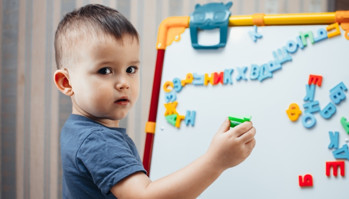 The little boy is studying the letters, using the easel with a magnetic surface.