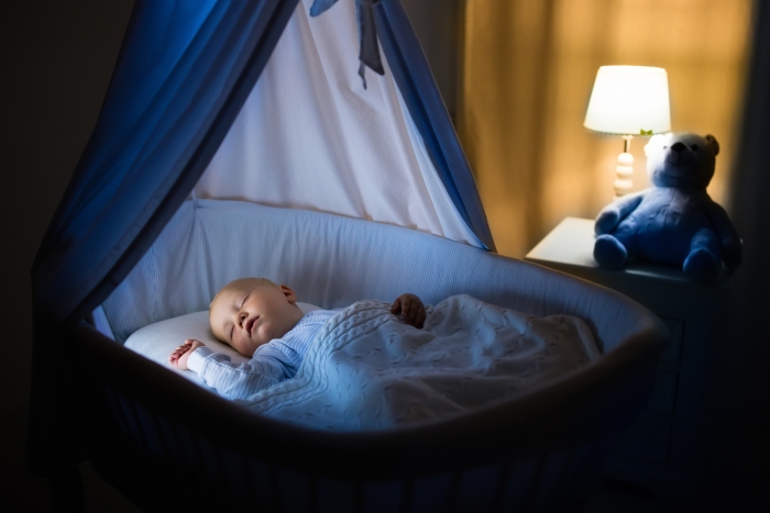 Adorable baby sleeping in blue bassinet with canopy at night.