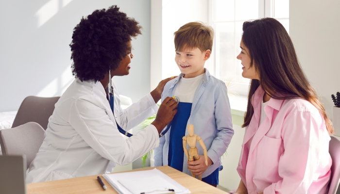 African female pediatrician examining boy patient with stethoscope.